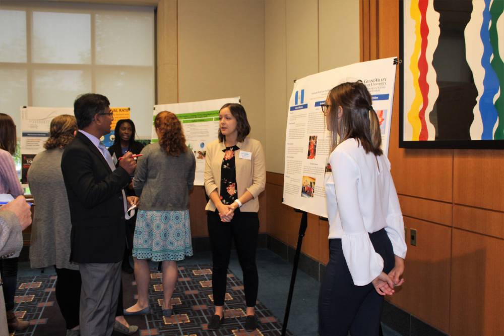 Image 1 of 15 A group of attendees standing around another poster presentation, asking questions